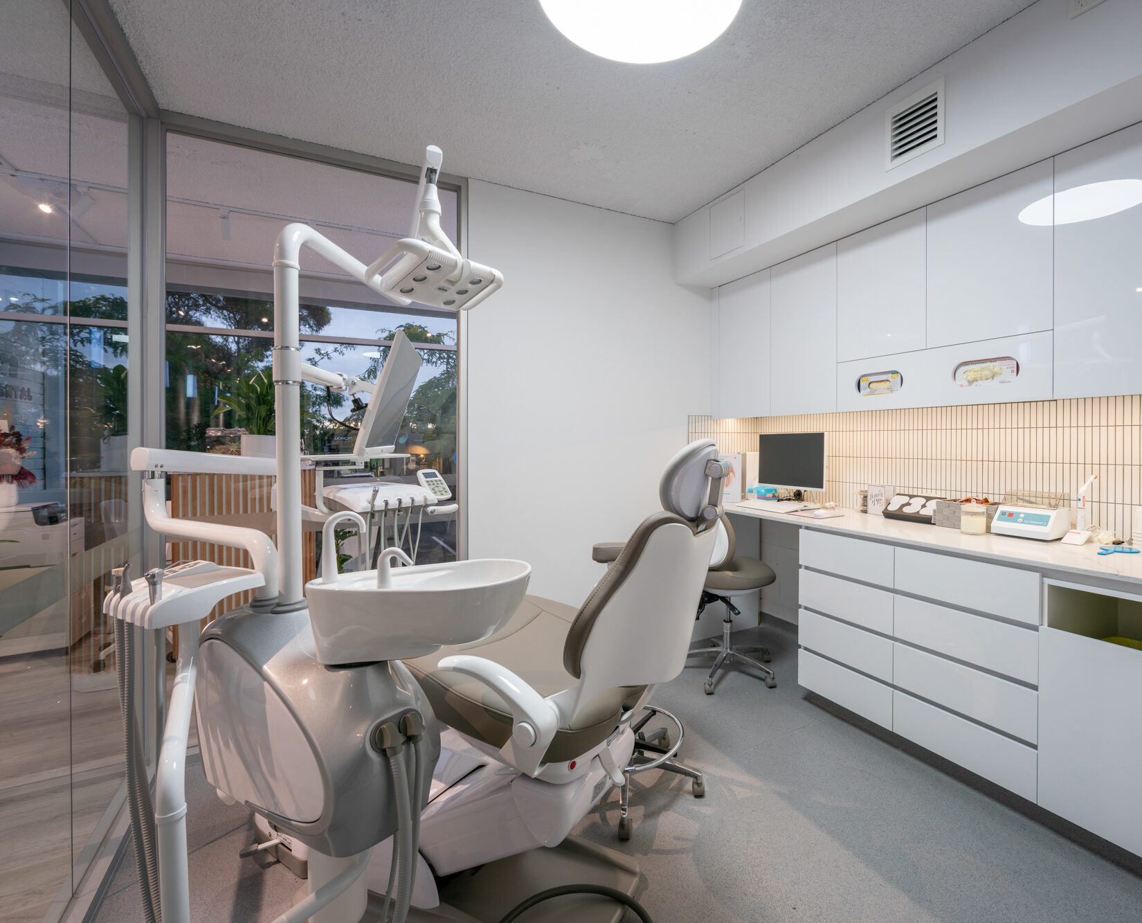 Modern dental chair with tan upholstery, an adjustable overhead light, and a white ceramic spittoon basin.