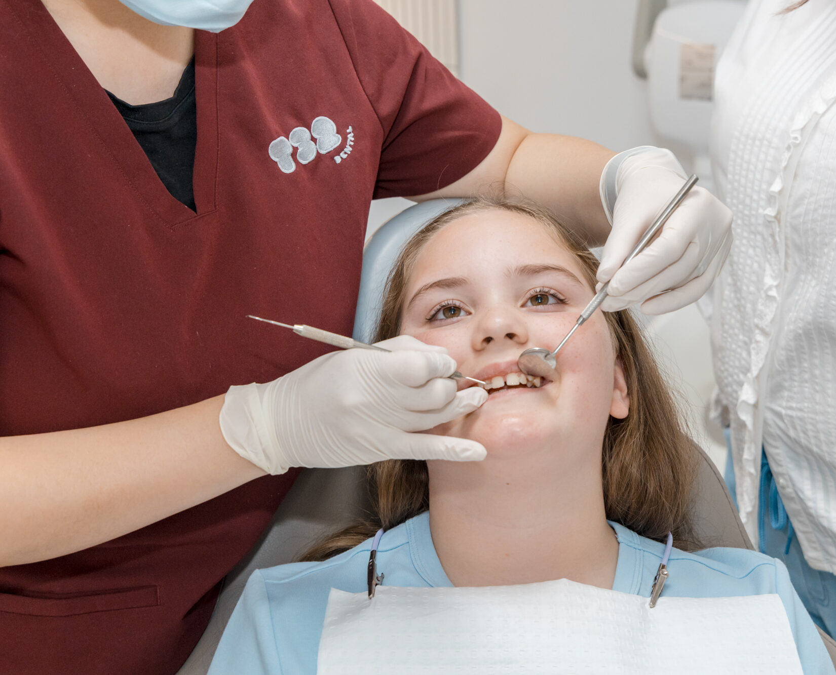 A dentist prepares a young girl's teeth for a scale cleaning procedure using dental mirror and probe.