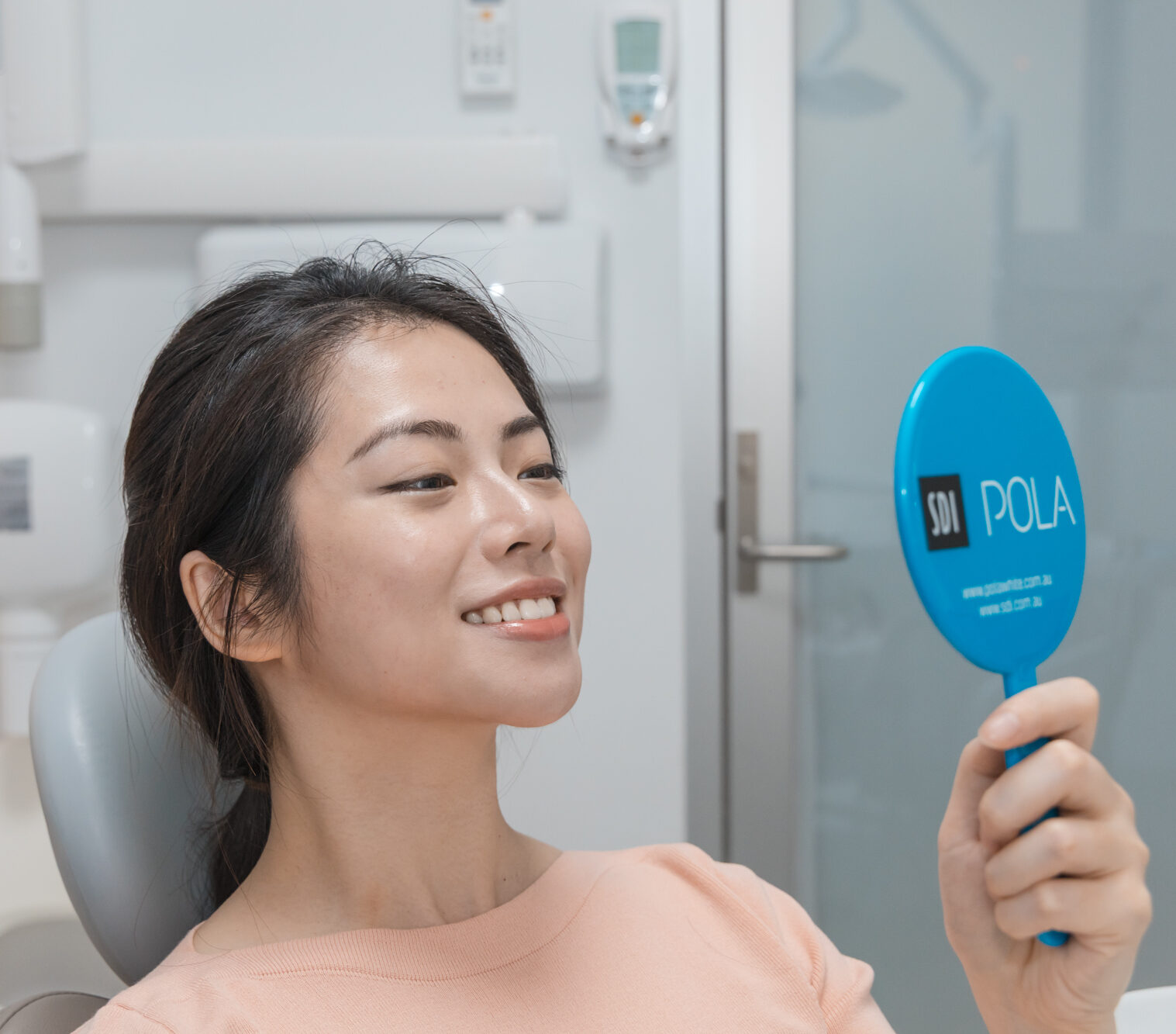 A patient smiles at her bright teeth in a mirror after a professional scale cleaning treatment.