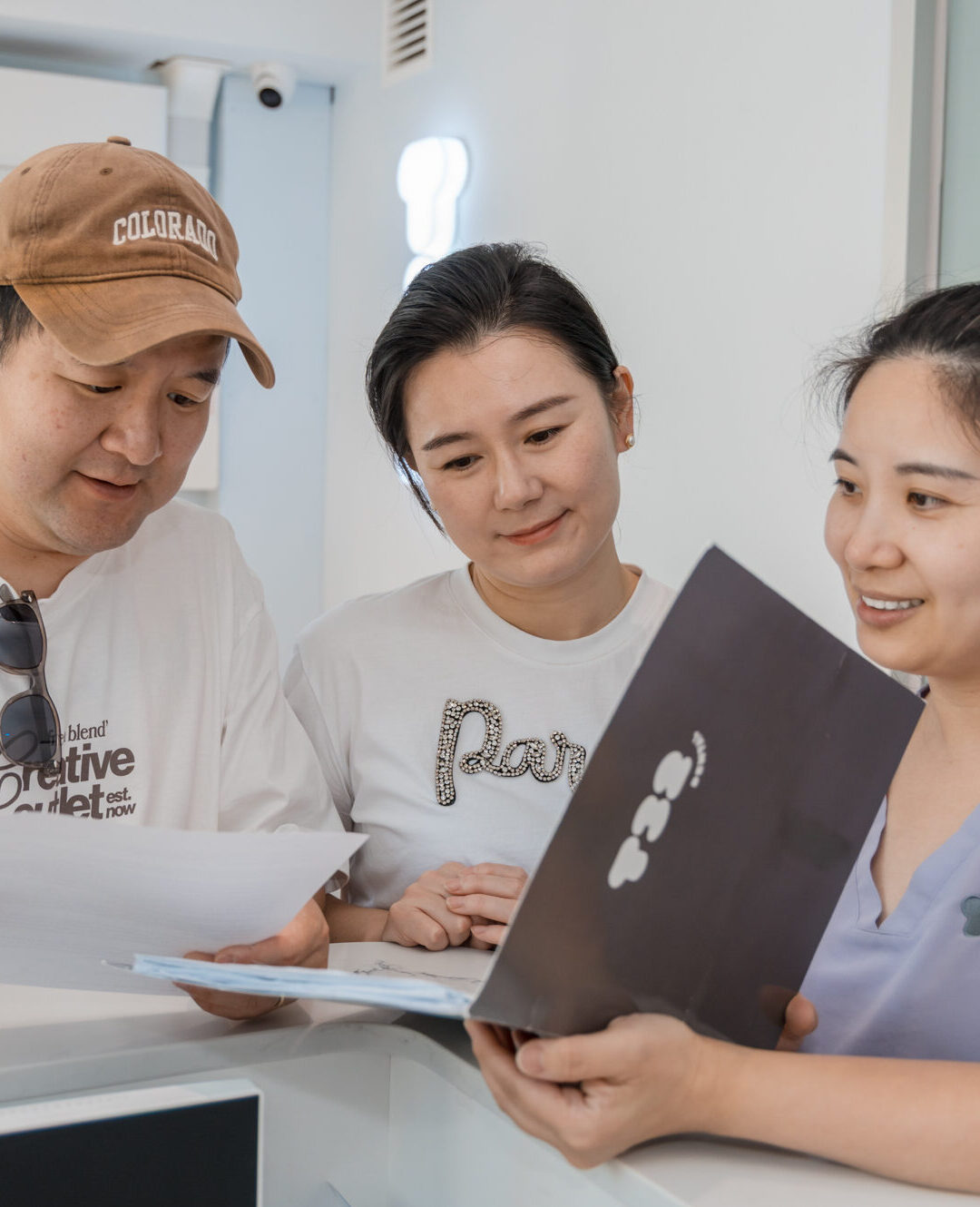 Dental nurse discussing composite veneers treatment options with a couple at a clinic reception desk.