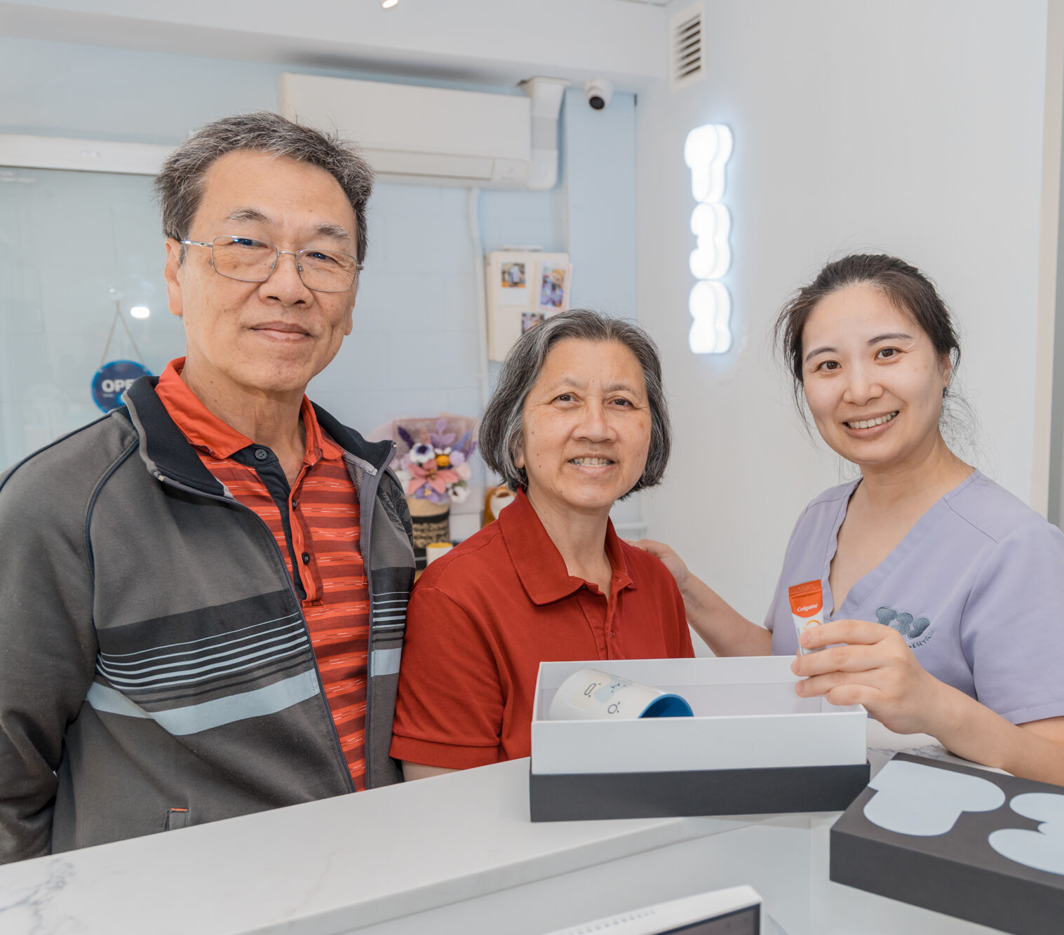 Happy patients at a clinic offering dental inlays and onlays receive a care package from a friendly staff member.