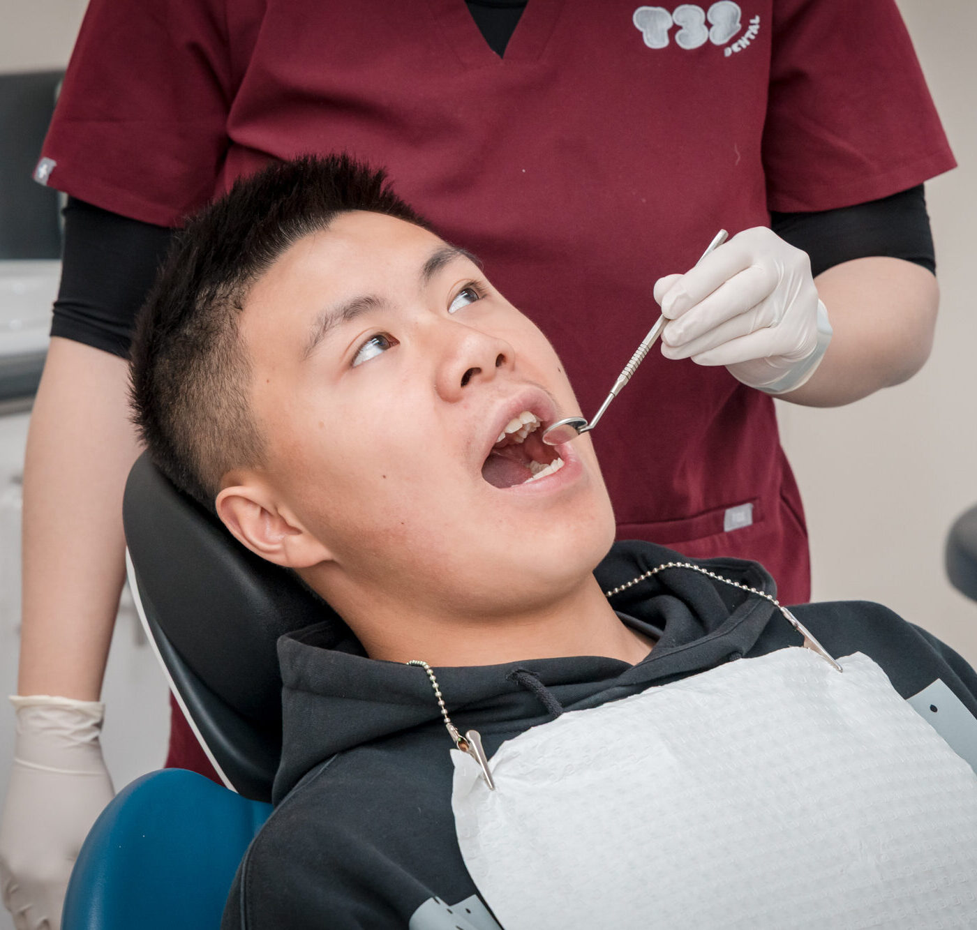 Dentist using a dental mirror tool to inspect the upper teeth of a reclined patient in a clinic.