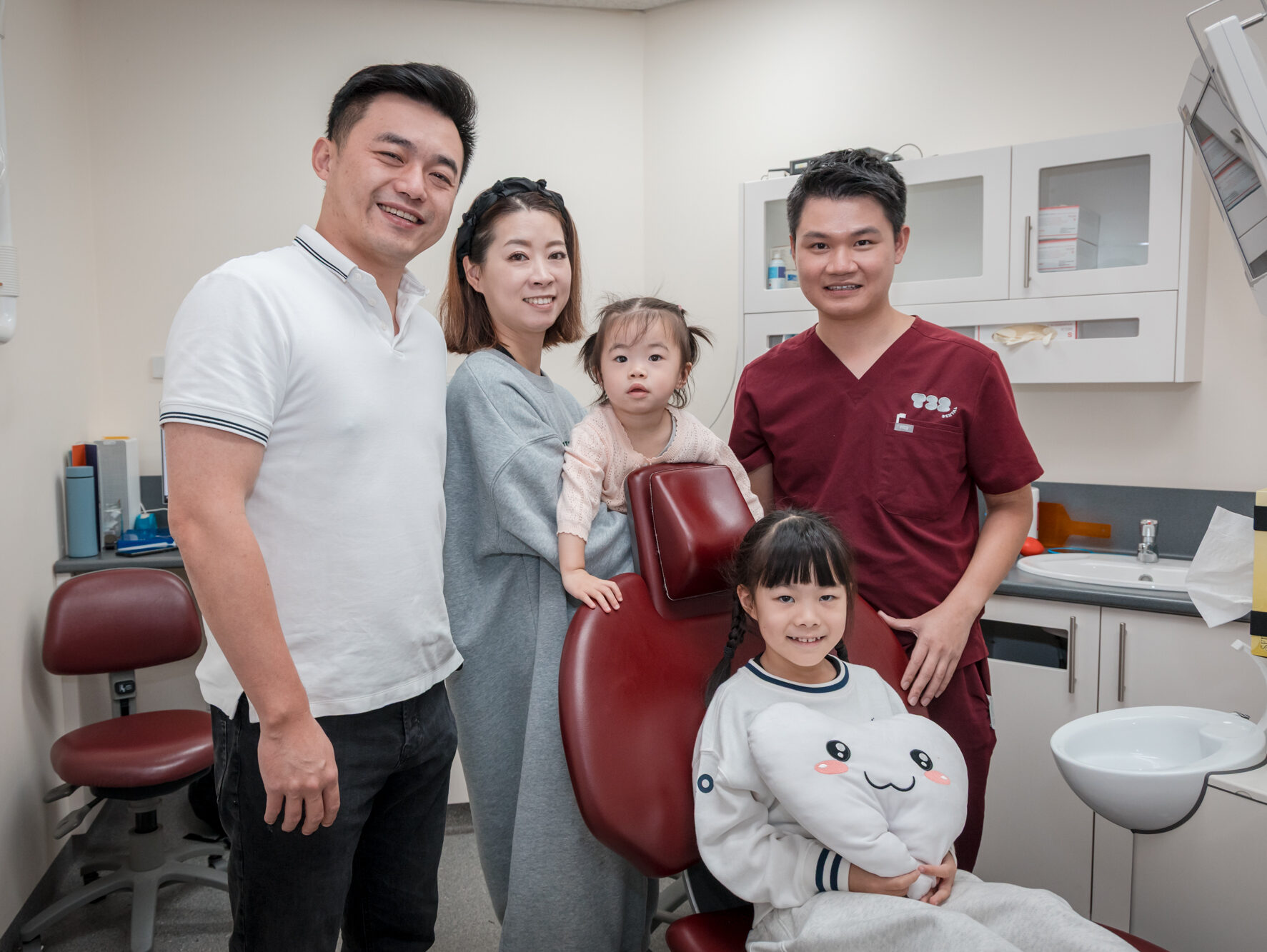 A family of four poses with a dentist in a clinic, with a young girl sitting in the dental chair holding a tooth plush.
