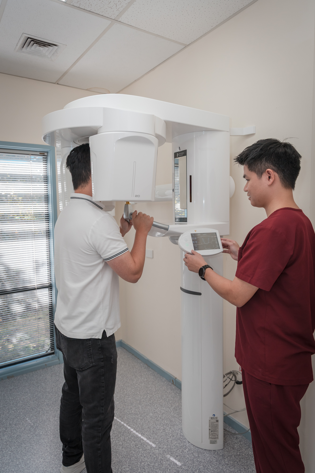 A patient receives a dental scan in preparation for a tooth extraction while a health professional operates the machine.