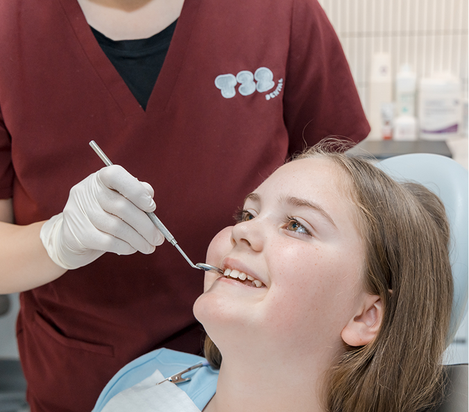 Dental professional checking a young patient's teeth for grinding wear before fitting protective night guards.