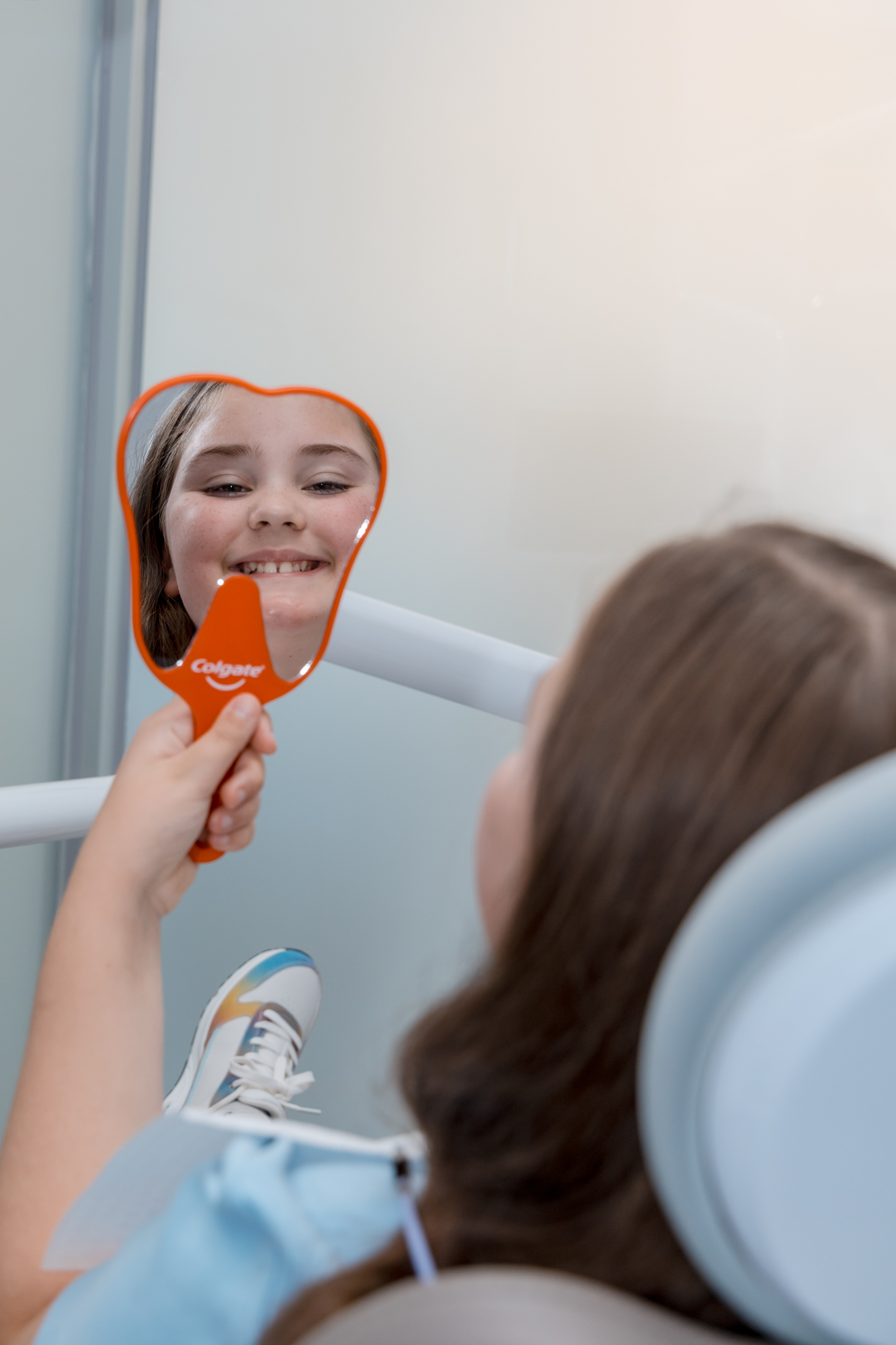 A young patient checks her beautiful smile in a mirror, showcasing composite veneers results.