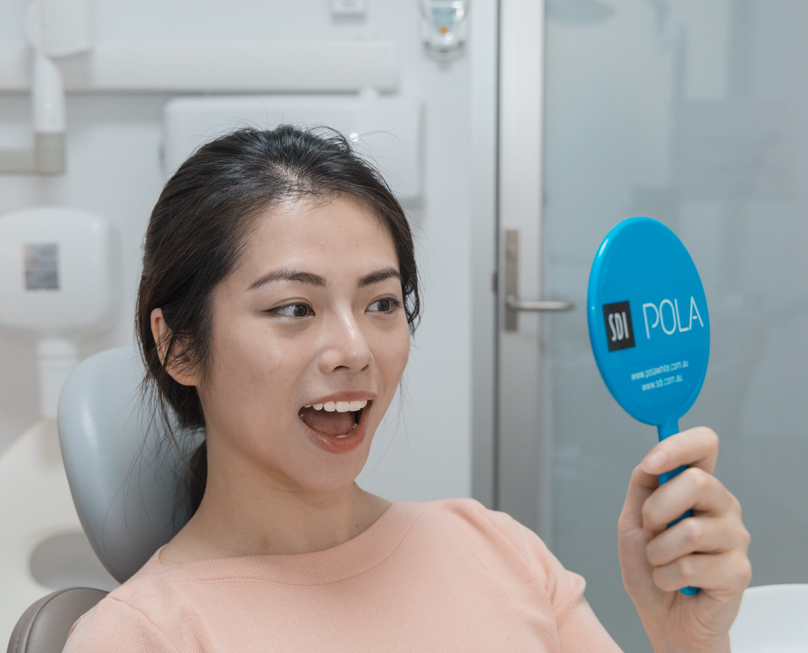Happy woman admiring her new smile in a mirror after a cosmetic dentistry treatment.